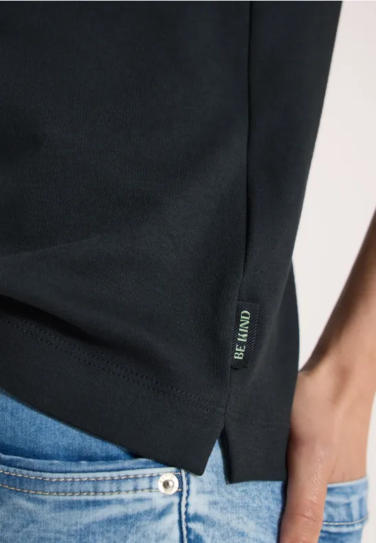 Close-up van een zwart t-shirt met zijsplit en klein logolabel, gecombineerd met een blauwe spijkerbroek.