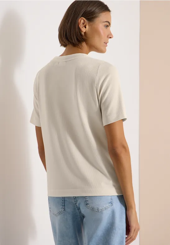 Rugaanzicht van een persoon met een beige T-shirt en lichte spijkerbroek voor een neutrale achtergrond.