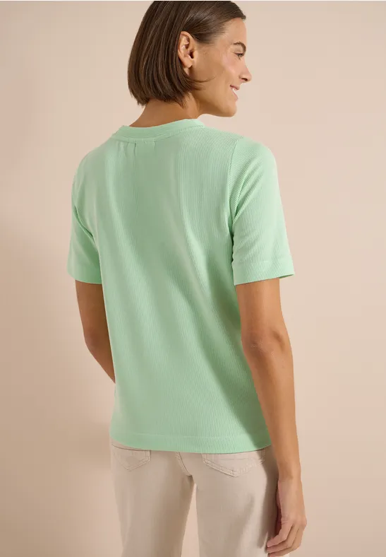 Achteraanzicht van een vrouw in een mintgroen t-shirt en lichte broek voor een neutrale achtergrond.