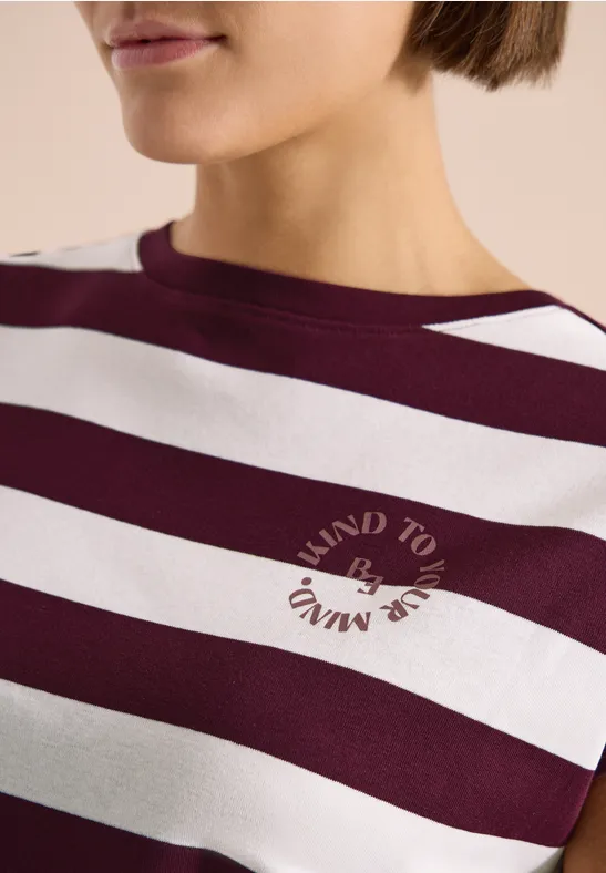 Nahaufnahme einer Frau in einem bordeaux-weißen, gestreiften Shirt mit rundem Schriftzug auf der Brust.