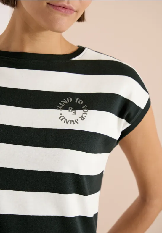 Eine Frau trägt ein kurzärmeliges Shirt mit breiten Schwarz-Weiß-Streifen und Kreislogo auf der Brust.