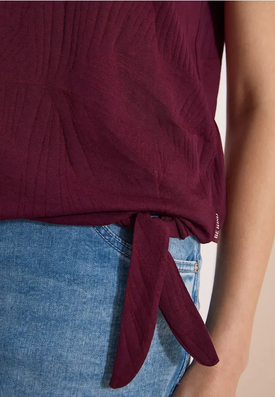 Haut féminin texturé couleur prune, noué sur le côté, porté avec un jean bleu.