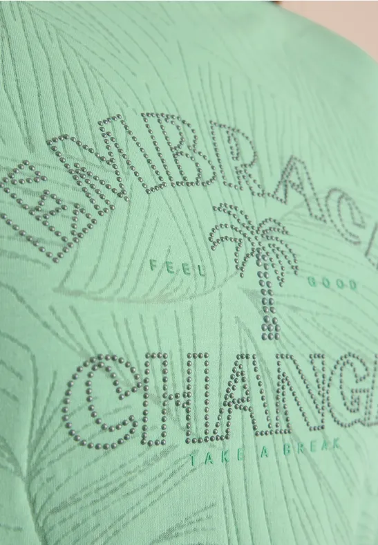 Grünes T-Shirt mit Strassschrift 'EMBRACE CHANGE', Palme in der Mitte und kleinem 'FEEL GOOD'-Schriftzug.