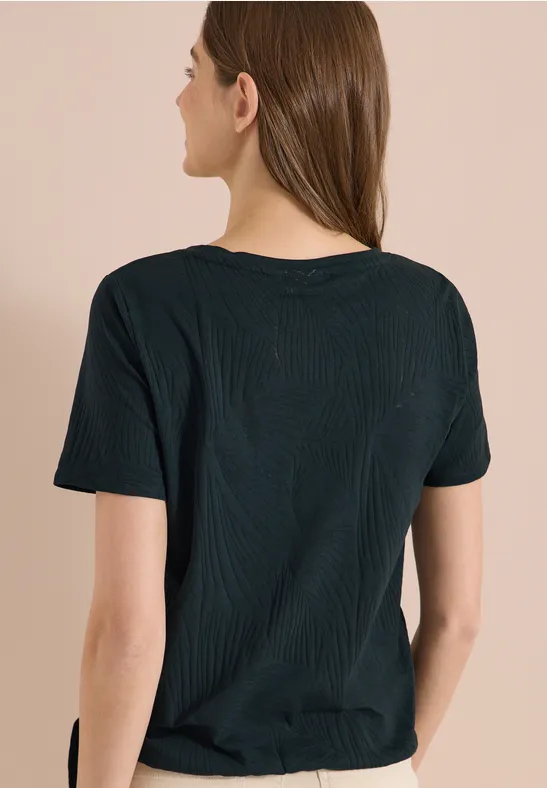 Frau steht mit dem Rücken zur Kamera und trägt ein schlichtes schwarzes T-Shirt.