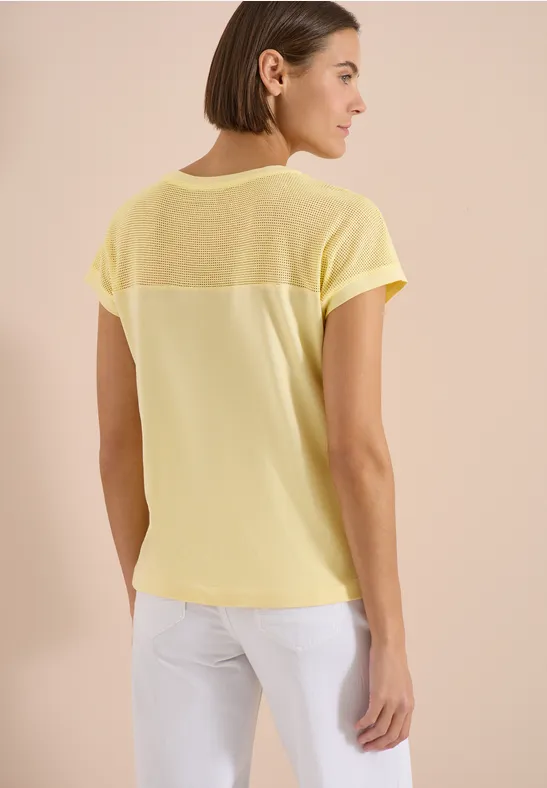 Vrouw van achteren in een losvallend geel T-shirt met transparante inzet op de rug.