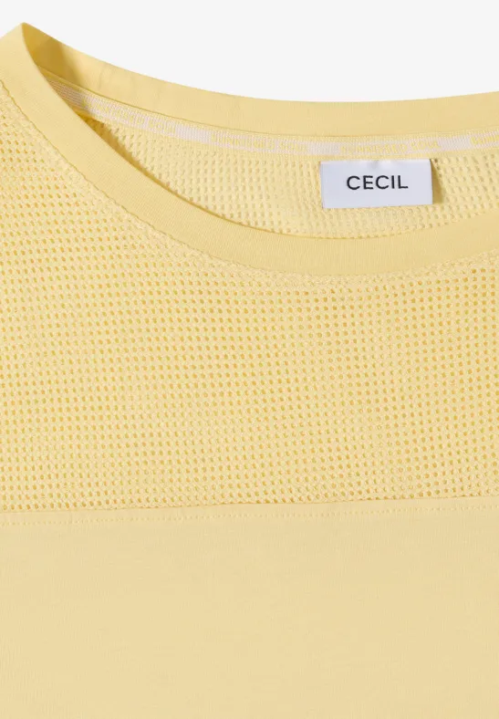 Close-up van een geel bovenstuk met mesh inzet bij de ronde hals, merklabel CECIL zichtbaar.