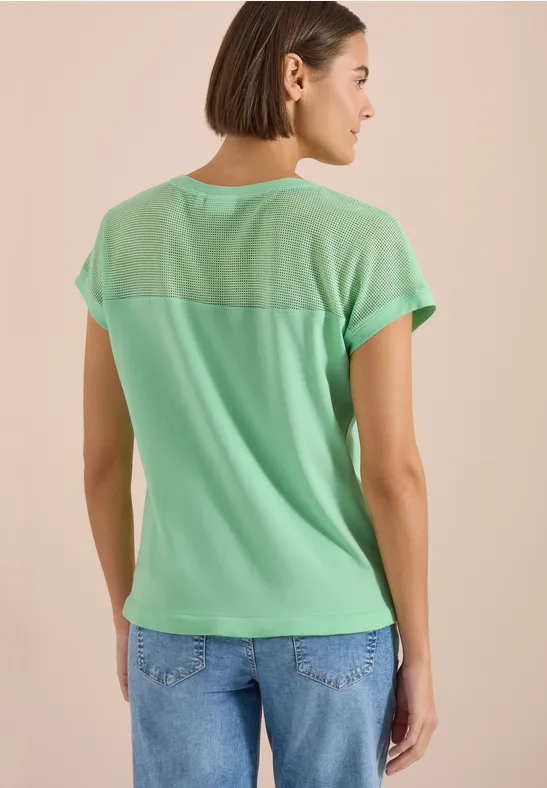 Frau von hinten in mintgrünem T-Shirt und blauen Jeans vor beigem Hintergrund.