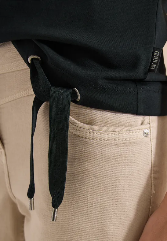 Een zwart hoodie met losse koorden over een beige spijkerbroek.
