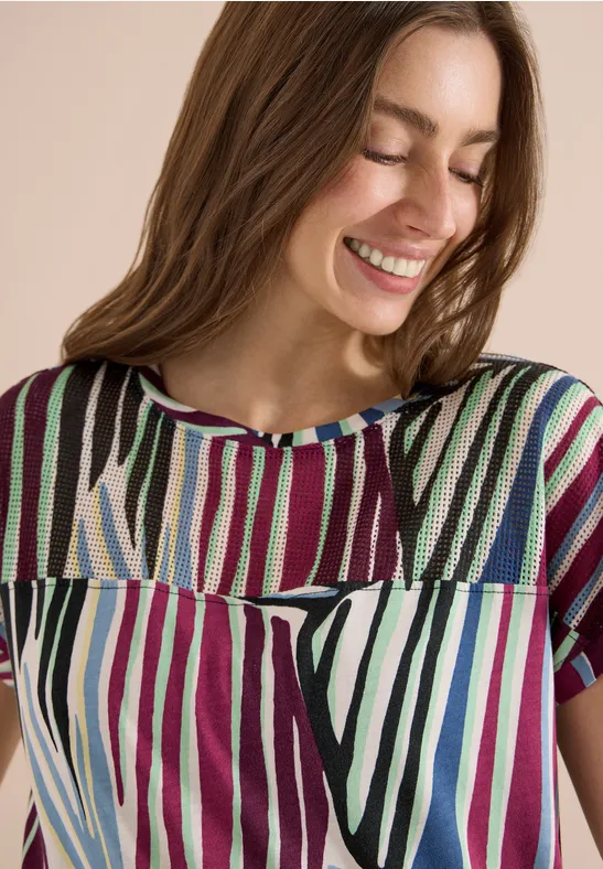 Femme porte un haut à manches courtes rayé verticalement de couleurs vives.