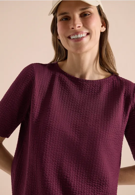 Vrouw draagt gestructureerd donkerpaars T-shirt met korte mouwen.