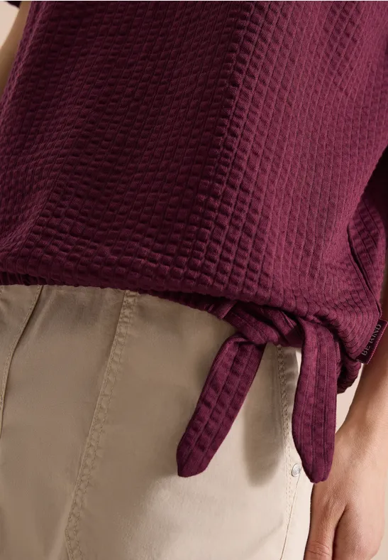 Donkerpaarse gewatteerde top met zijstrik, gecombineerd met beige broek.