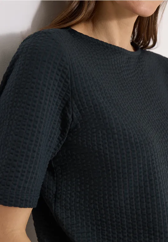Vrouw draagt zwart, kort mouwig topje met wafelstructuur en ronde hals.