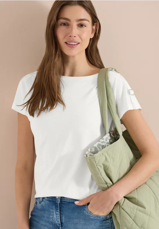 Frau trägt weißes T-Shirt, blaue Jeans und eine grüne, gesteppte Schultertasche.