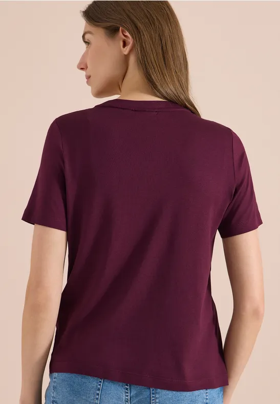 Eine Frau von hinten in lila T-Shirt und Jeans.