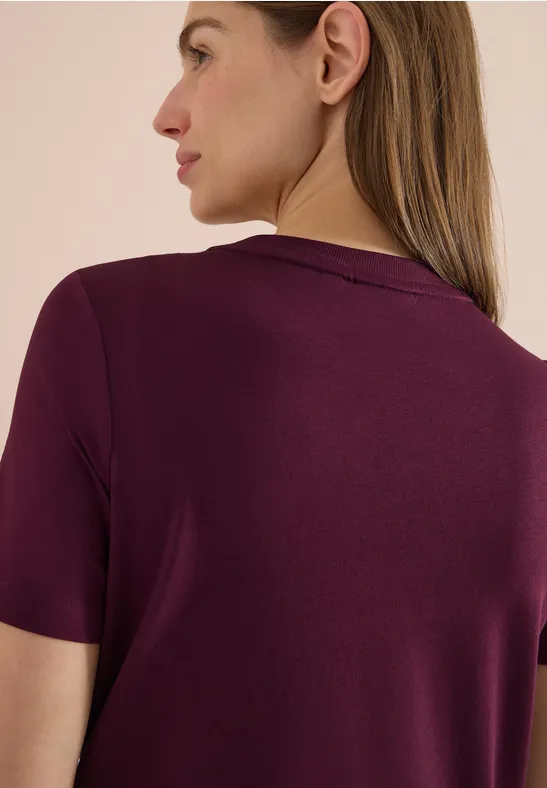 Verschwommene Frau von hinten trägt ein kurzärmeliges, bordeauxrotes Oberteil.