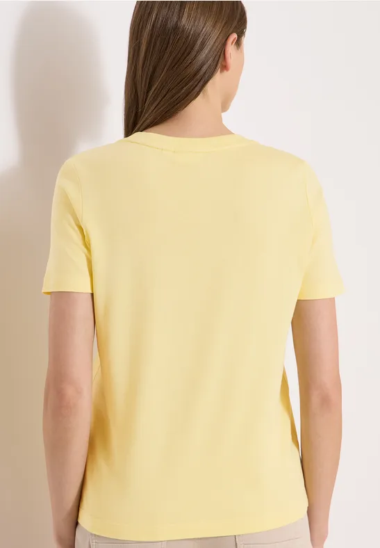 Vue de dos d'une femme portant un t-shirt jaune à manches courtes sur fond neutre.