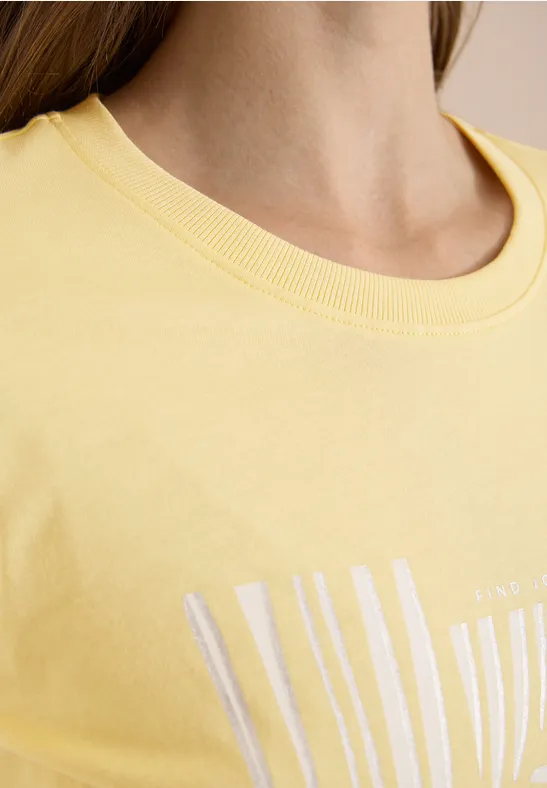 Gros plan d’un buste en t-shirt jaune à col rond avec motif blanc.