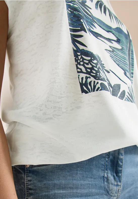 Seitliche Ansicht einer Person mit weißem Shirt mit Tropen-Print und blauen Jeans.