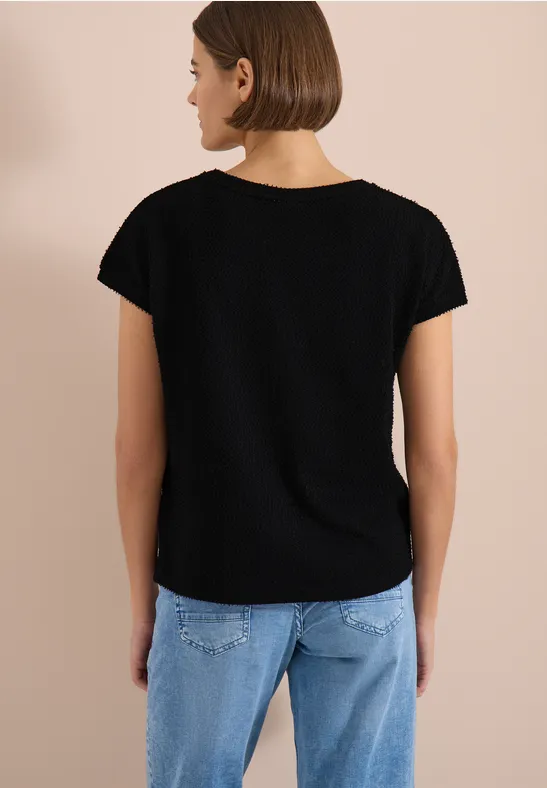 Frau von hinten in schwarzem T-Shirt und hellblauen Jeans vor beigefarbenem Hintergrund.