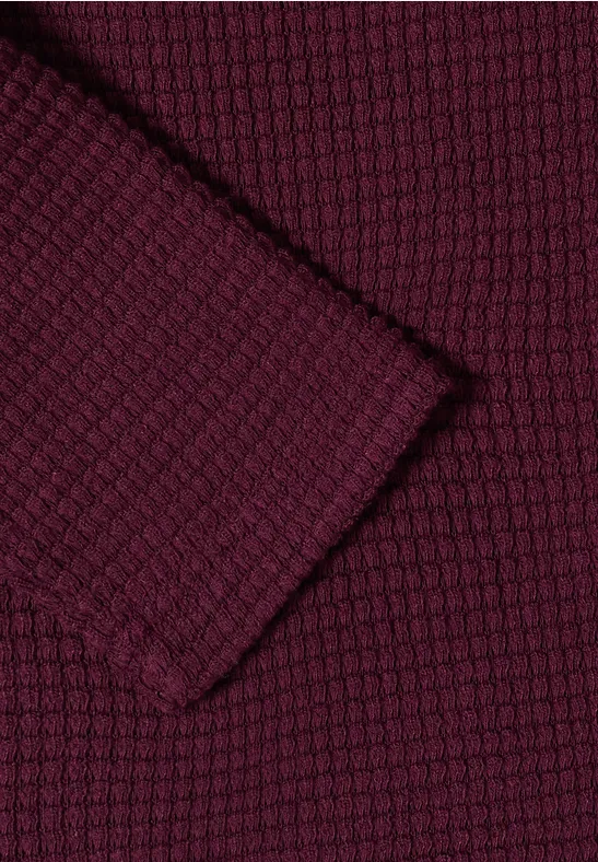 Gros plan d'un tissu tricoté bordeaux à motif nid d'abeille texturé.