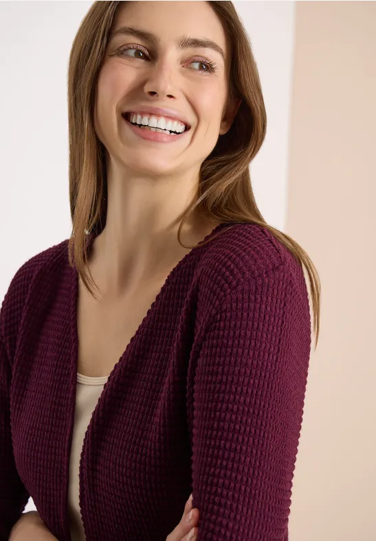 Femme portant un gilet violet sur un débardeur blanc devant un fond neutre