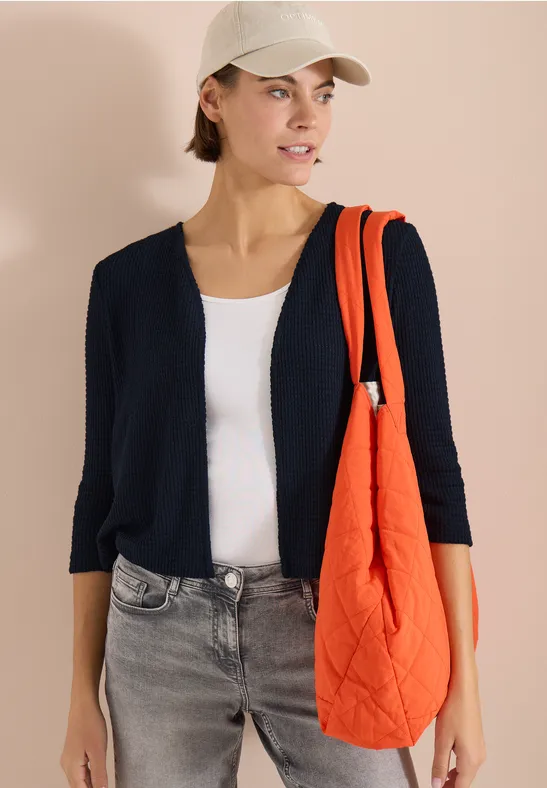 Modisches Model in dunkelblauer Strickjacke, weißem Top, grauen Jeans und orangefarbener gesteppten Tasche