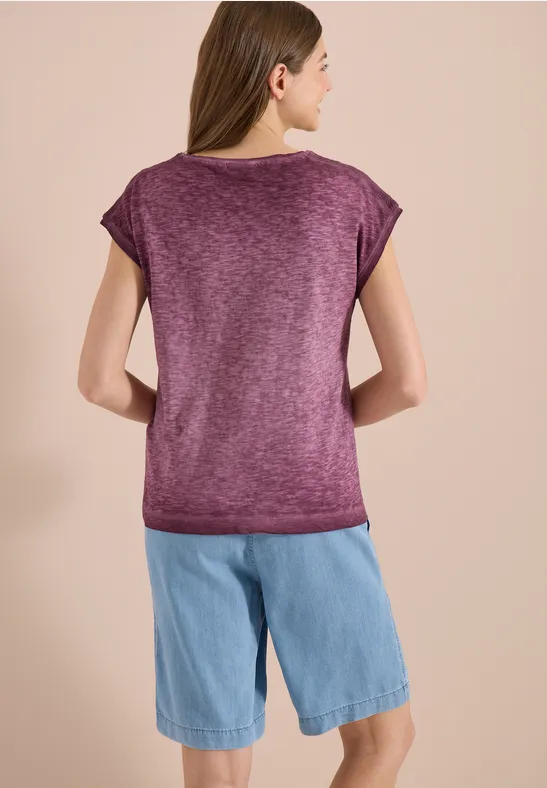 Een vrouw van achteren, gekleed in een paarse T-shirt en blauwe spijkershorts.