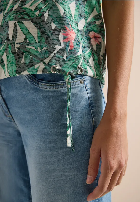 Persoon draagt blauwe jeans en groene top met print en zijstrikje