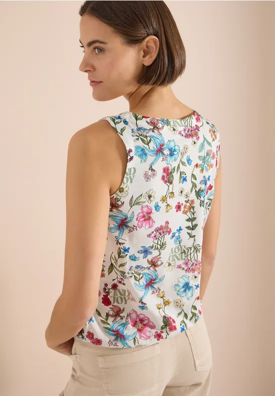 Frau von hinten in ärmellosem weißen Top mit buntem Blumenprint und hellen Hosen.