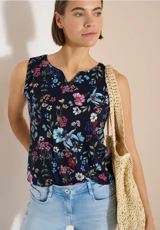 Femme portant un haut sans manches bleu foncé à imprimé fleuri coloré et un sac en paille.