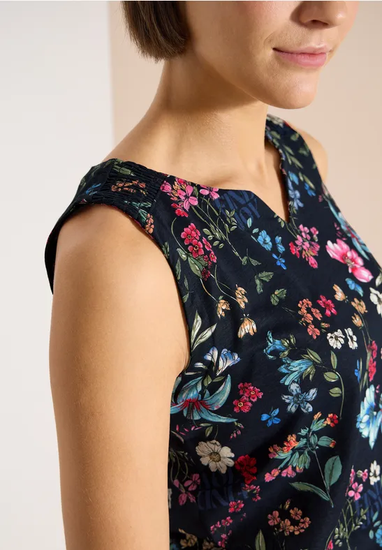 Gros plan d'une femme portant un haut sans manches noir orné de motifs floraux colorés.
