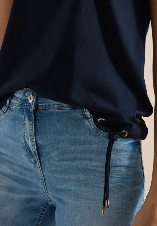 Nahaufnahme: Person trägt blaue Jeans mit Kordelzug an der Taille und dunkelblaues Oberteil.