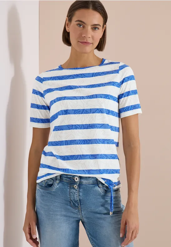 Personne devant un mur clair, vêtue d'un t-shirt rayé bleu et blanc et d'un jean bleu.