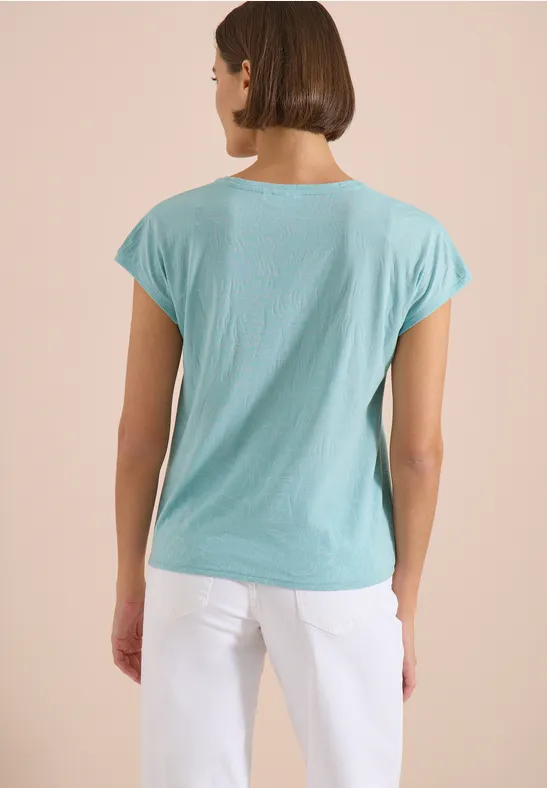 Frau von hinten in hellblauem T-Shirt und weißer Hose.