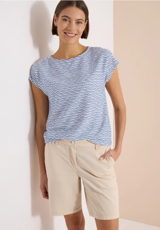 Femme vêtue d’un t-shirt rayé bleu et blanc et d’un short beige, main dans la poche.