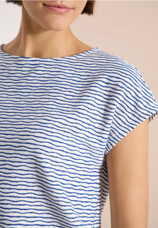Haut du corps d'une personne portant un t-shirt blanc à fines rayures bleues et manches courtes.