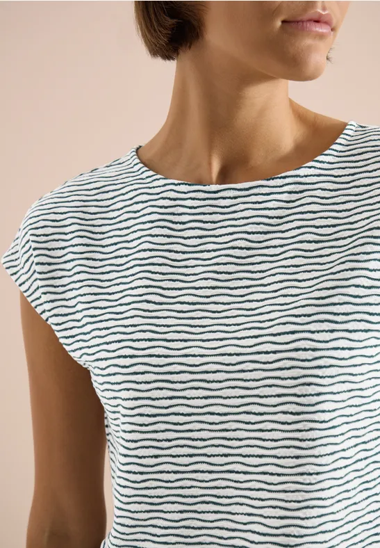Plan rapproché d'une femme en t-shirt blanc simple à fines rayures ondulées noires.