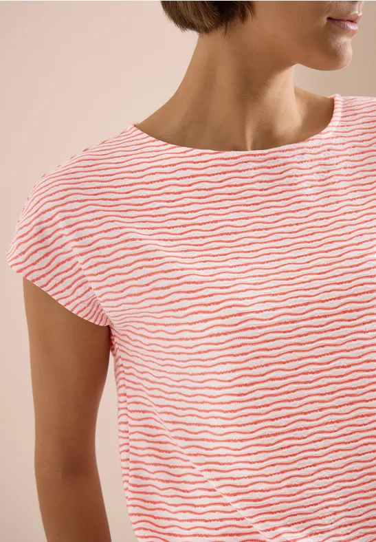 Femme portant un t-shirt blanc à fines rayures orange, manches courtes et col rond, sur fond beige