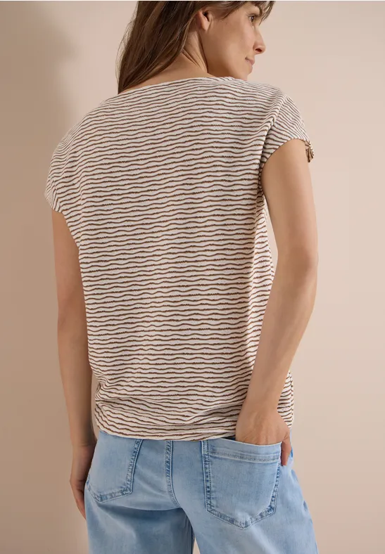 Vrouw van achteren in gestreept T-shirt en spijkerbroek, handen in de zakken.