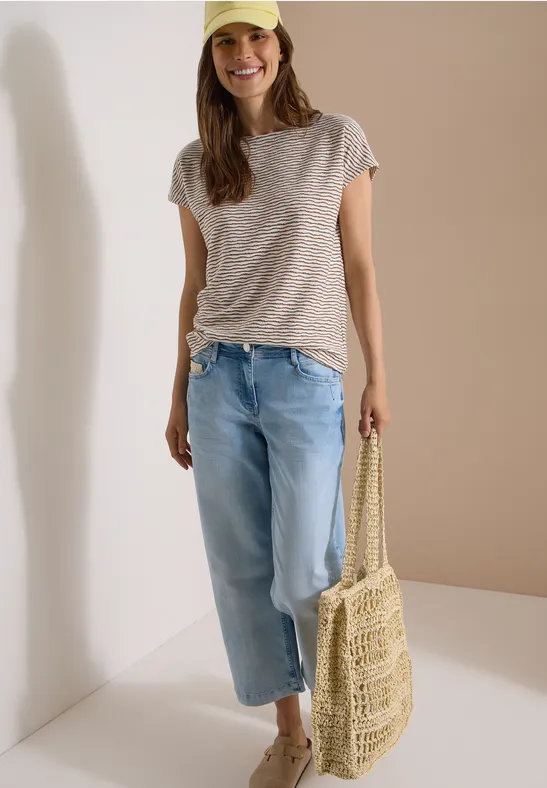 Vrouw in gestreept shirt, wijde spijkerbroek en gevlochten rieten tas.