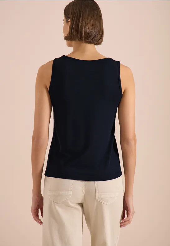 Femme de dos portant un top bleu marine sans manches et un pantalon clair