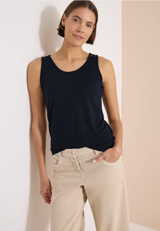 Une personne mince porte un débardeur bleu foncé et un pantalon beige sur fond clair.