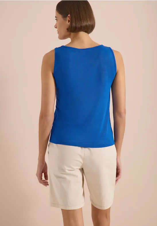 Frau von hinten in blauem Top und hellen Shorts vor neutralem Hintergrund.