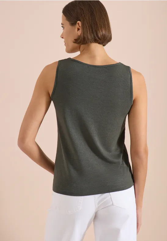 Femme vue de dos, portant un débardeur gris foncé et un pantalon blanc devant un mur beige