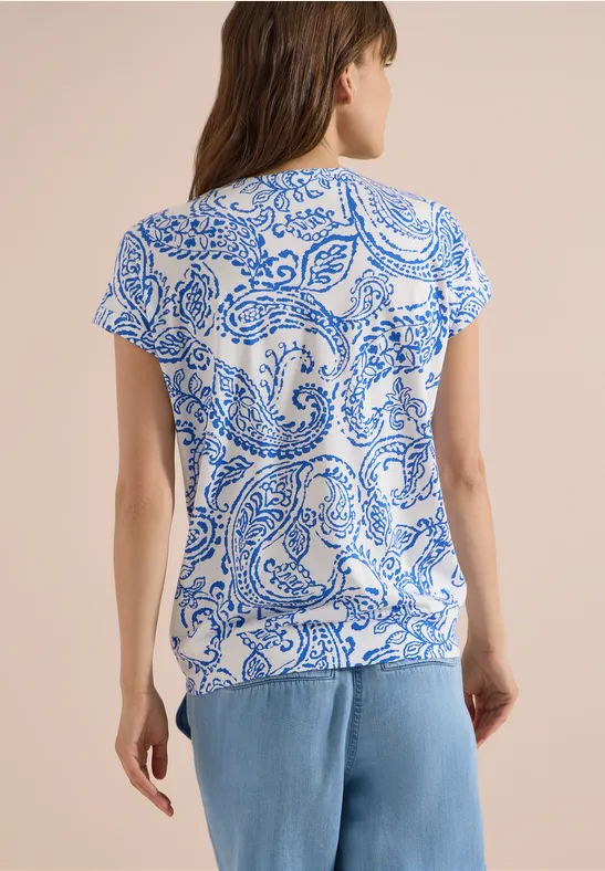 Vrouw van achteren in een wit t-shirt met blauw patroon en een lichtblauwe spijkerbroek.