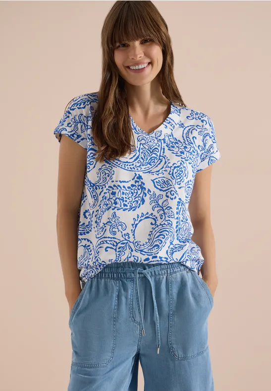 Vrouw draagt blauw-wit patroon T-shirt met korte mouwen en lichtblauwe broek met zakken en trekkoord.