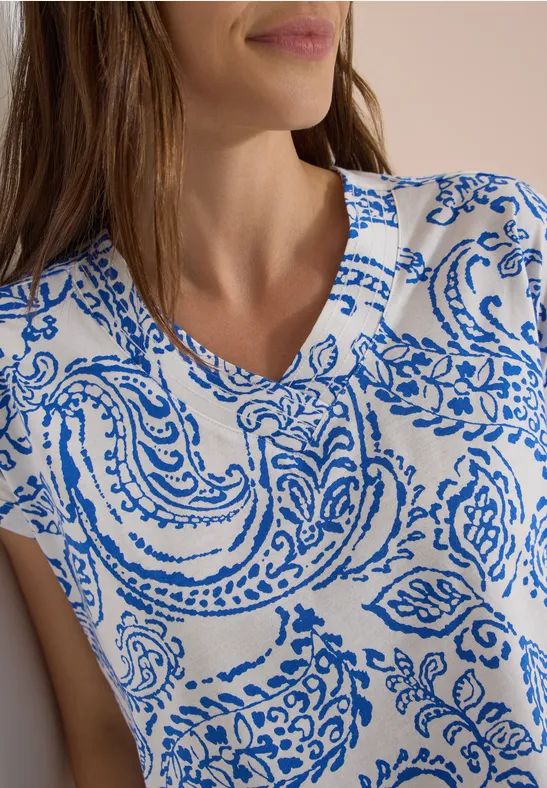 Vrouw draagt een wit shirt met blauw paisley-patroon en V-hals.