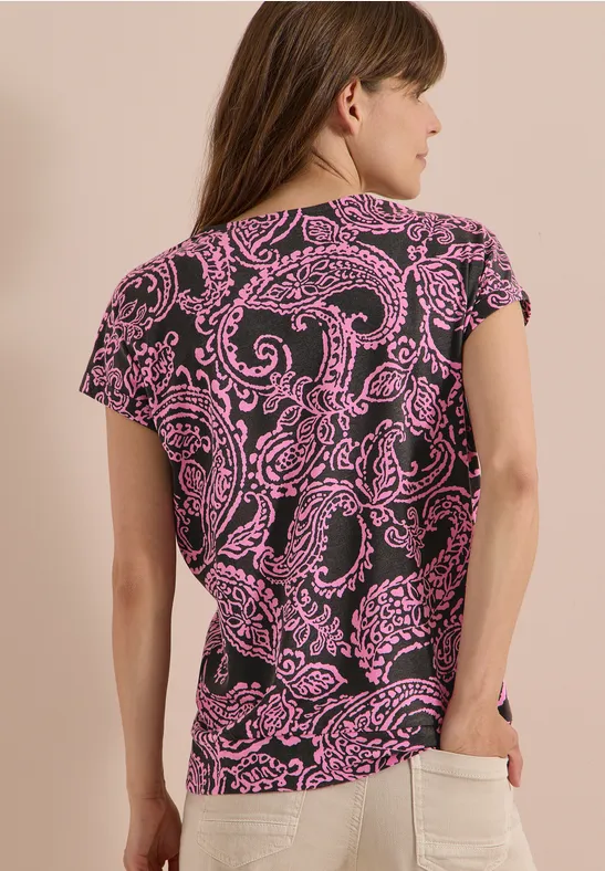 Frau von hinten in schwarzem T-Shirt mit pinkem Paisleymuster und Jeans mit aufgesetzter Tasche.
