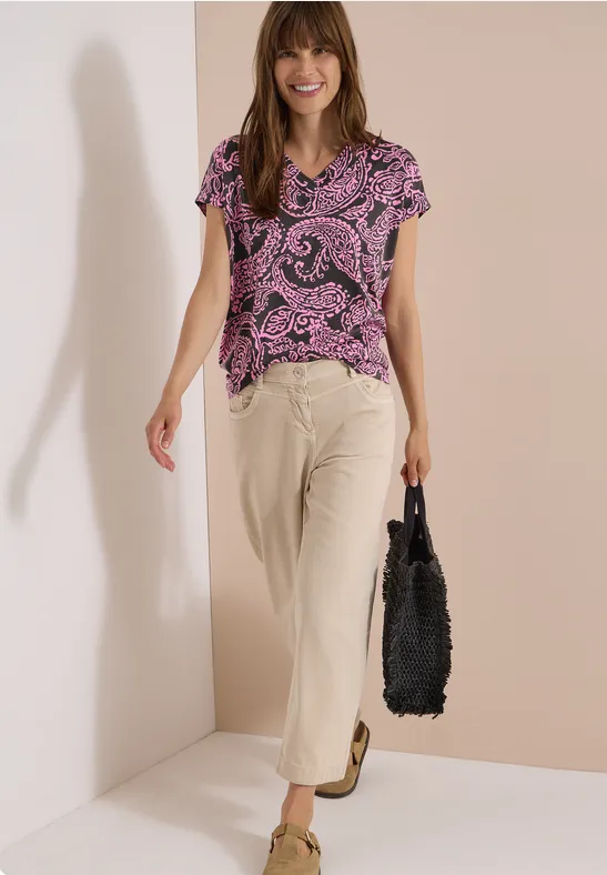 Frau trägt lila Paisley-Shirt, beige Hose und schwarze Tasche.