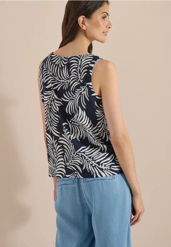 Femme vue de dos portant un haut sans manches bleu marine à motif de feuilles blanches et un jean clair.